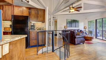 A spacious kitchen with wooden cabinets and a black refrigerator, a living area with a leather sofa, and a balcony with a view.