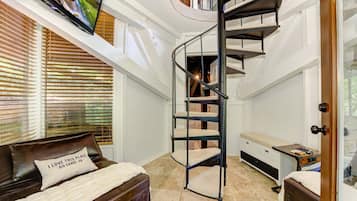 A bedroom with a spiral staircase, a bed with a pillow, a desk, and a TV mounted on the wall.