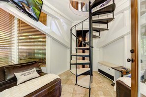 A bedroom with a spiral staircase, a bed with a pillow, a desk, and a TV mounted on the wall.