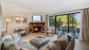 Un salon chaleureux avec une cheminée, des sièges confortables et une grande fenêtre donnant sur l’extérieur.