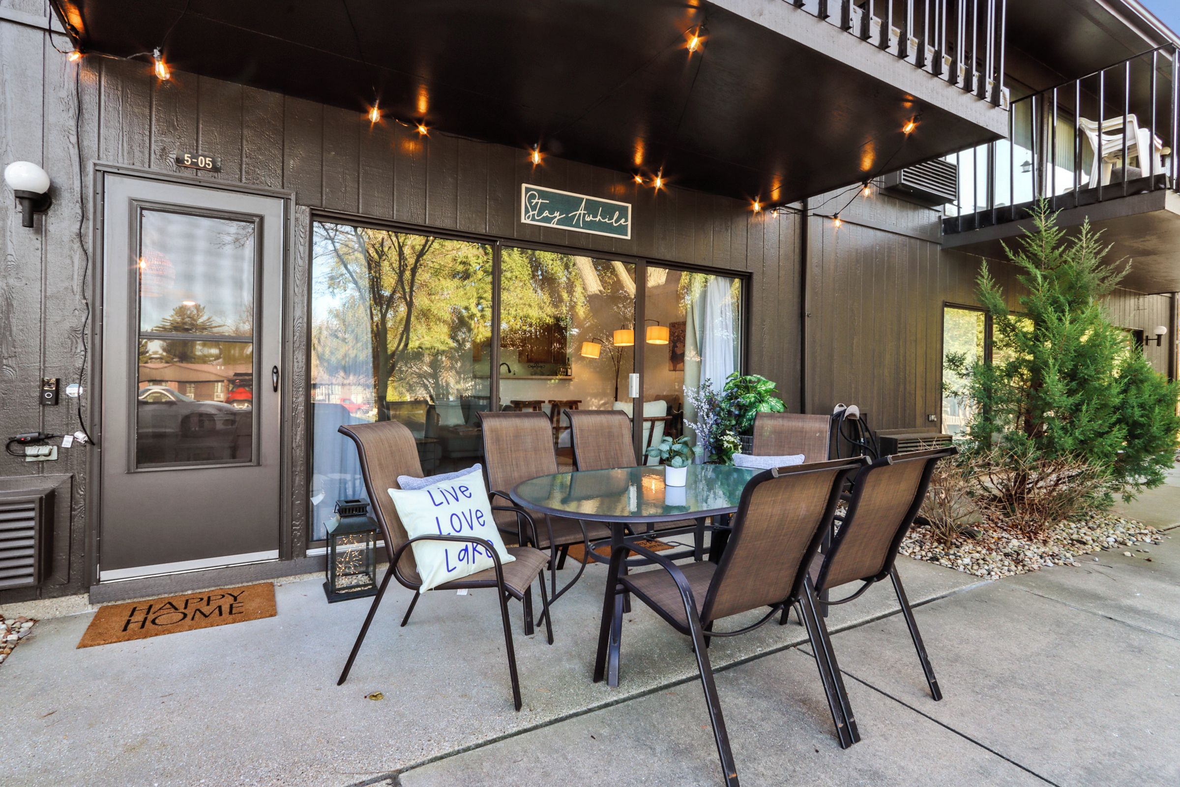 An outdoor seating area with a glass table and chairs, a sign reading 'Stay Awake,' and a door marked '5-05.'