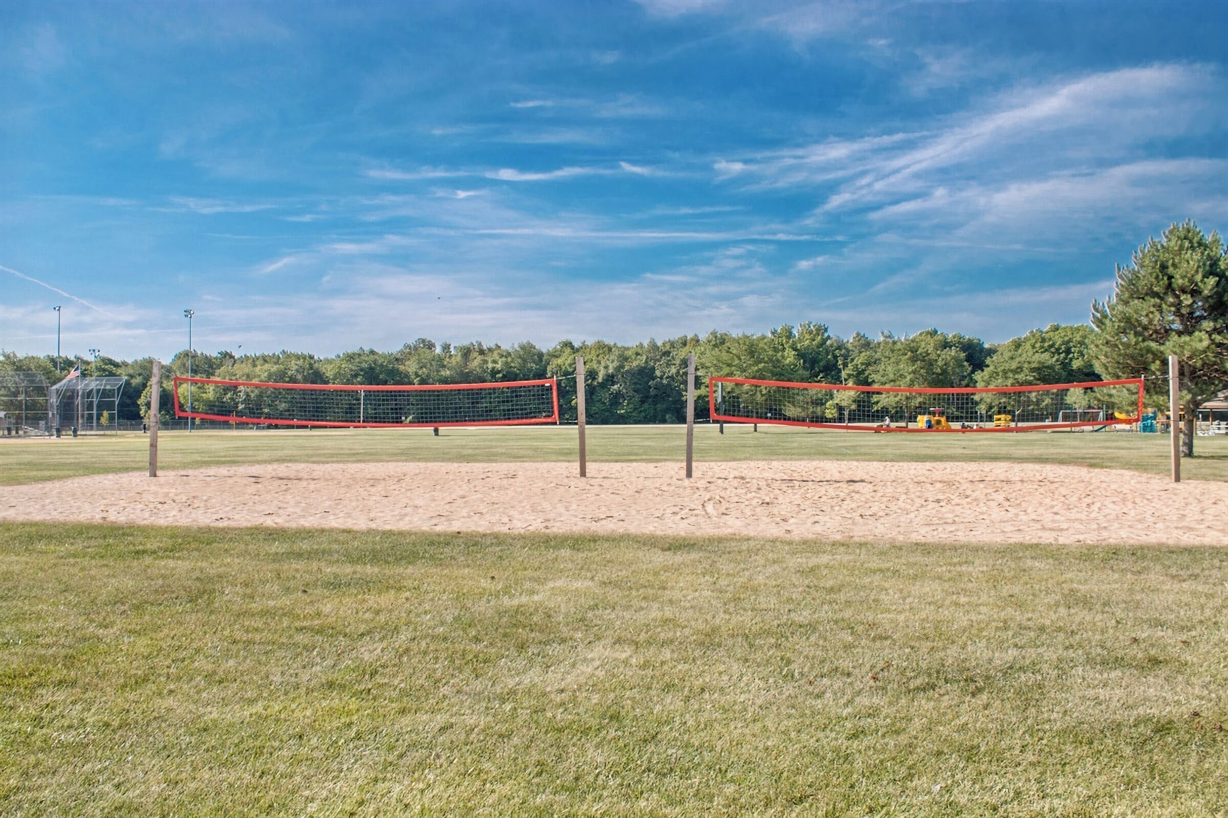 Cancha de voleibol con red, rodeada por un campo de césped y árboles.