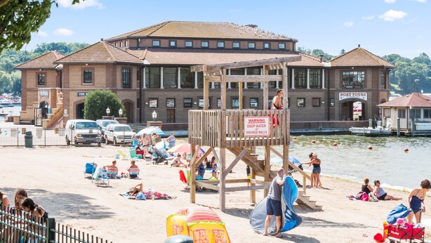 Une plage avec un poste de surveillance pour les sauveteurs, un bâtiment avec une enseigne indiquant «Excursions en bateau», et une vue dégagée sur l’eau.