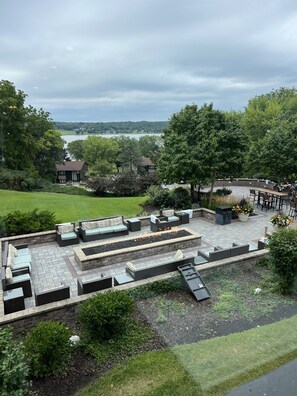 Een terras met buitenmeubilair en een vuurplaats, omgeven door groen en met uitzicht op een waterpartij.