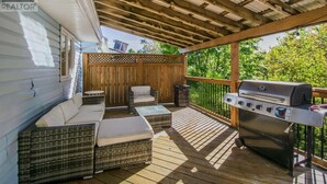 A covered outdoor deck with wicker furniture, a grill, and a wooden fence. - Cozy & Spacious 2BR home in a quiet neighborhood near shopping center (Lower Sackville)