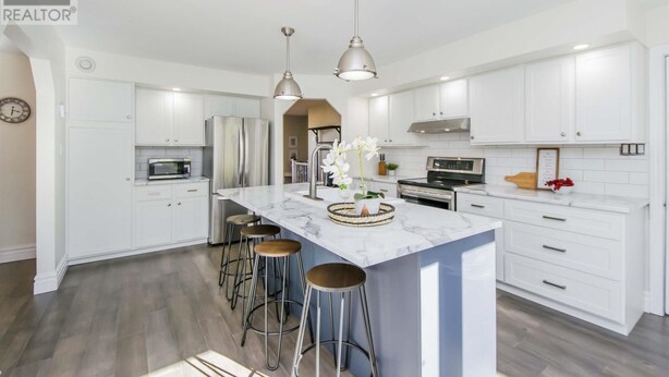 A modern kitchen with white cabinets, stainless steel appliances, a marble island, and bar stools. - Cozy & Spacious 2BR home in a quiet neighborhood near shopping center (Lower Sackville)