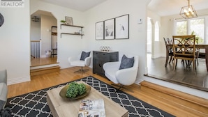 A spacious living room with a dining area, featuring a modern chandelier, white leather chairs, and a wooden dining table. - Cozy & Spacious 2BR home in a quiet neighborhood near shopping center (Lower Sackville)