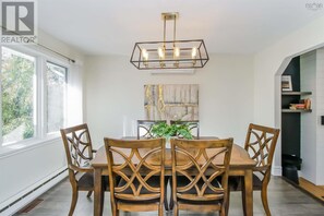 Un comedor con una mesa y sillas de madera, una lámpara colgante y un cuadro en la pared.