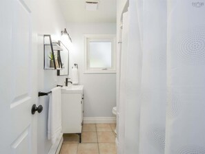Un couloir étroit mène à une salle de bain équipée d’un lavabo blanc, d’un miroir et de toilettes.