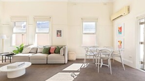 A modern living room with a sofa, coffee table, and dining area. - Oversized Artdeco Apartment w 4m high ceilings (Glebe)