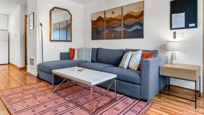 A modern living room with a grey sofa, a white coffee table, a patterned rug, and wall art depicting a sunset. - 08 Lodge, Downtown, AC, Ground Floor, Hood River! (Hood River)