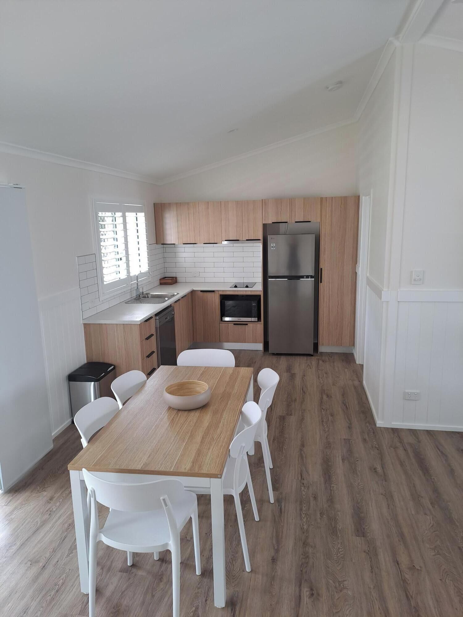 Una cocina moderna con armarios de madera, un refrigerador de acero inoxidable y un comedor con mesa de madera y sillas blancas.