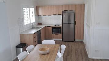 Una cocina moderna con armarios de madera, un refrigerador de acero inoxidable y un comedor con mesa de madera y sillas blancas.