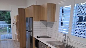 Eine moderne Küche mit Holzschränken, einem Edelstahlkühlschrank, einem Geschirrspüler und einem Fenster mit Jalousien.