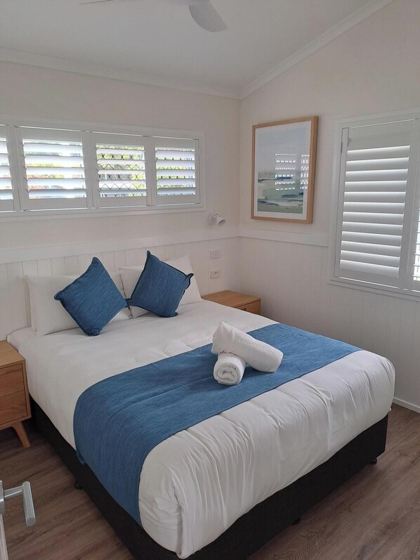 A neatly made bed with a blue and white bedspread, two blue pillows, and a rolled towel on the bed.