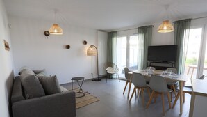 A modern living room with a sofa, dining table, chairs, and a TV. - Reflet du Parmelan Annecy (Annecy)