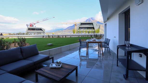 A modern outdoor patio with a sofa, dining table, and chairs. A construction crane is visible in the background. - Reflet du Parmelan Annecy (Annecy)
