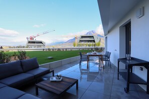 A modern outdoor patio with a sofa, dining table, and chairs. A construction crane is visible in the background. - Reflet du Parmelan Annecy (Annecy)