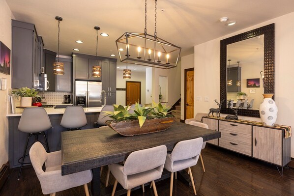 Una cocina moderna con armarios de madera oscura, una isla central con sillas, iluminación colgante y un espejo grande sobre la isla.