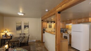 Une cuisine compacte avec des meubles en bois, un réfrigérateur blanc et un coin repas comprenant une table et des chaises.