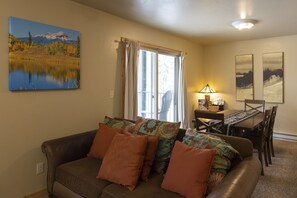 A living room with a brown leather couch, a dining table with chairs, a lamp, and two framed pictures on the wall. - Purgatory Townhomes 151 - Walking distance to Lift (Durango)