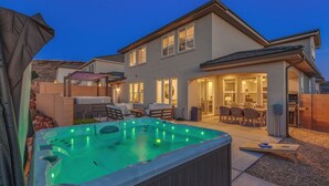 Ein zweistöckiges Haus mit Whirlpool im Garten, einer überdachten Terrasse und einem gut beleuchteten Innenraum.