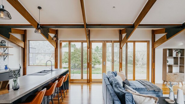 A modern kitchen with a bar area, a dining space with a sofa, and large sliding glass doors leading to a garden.