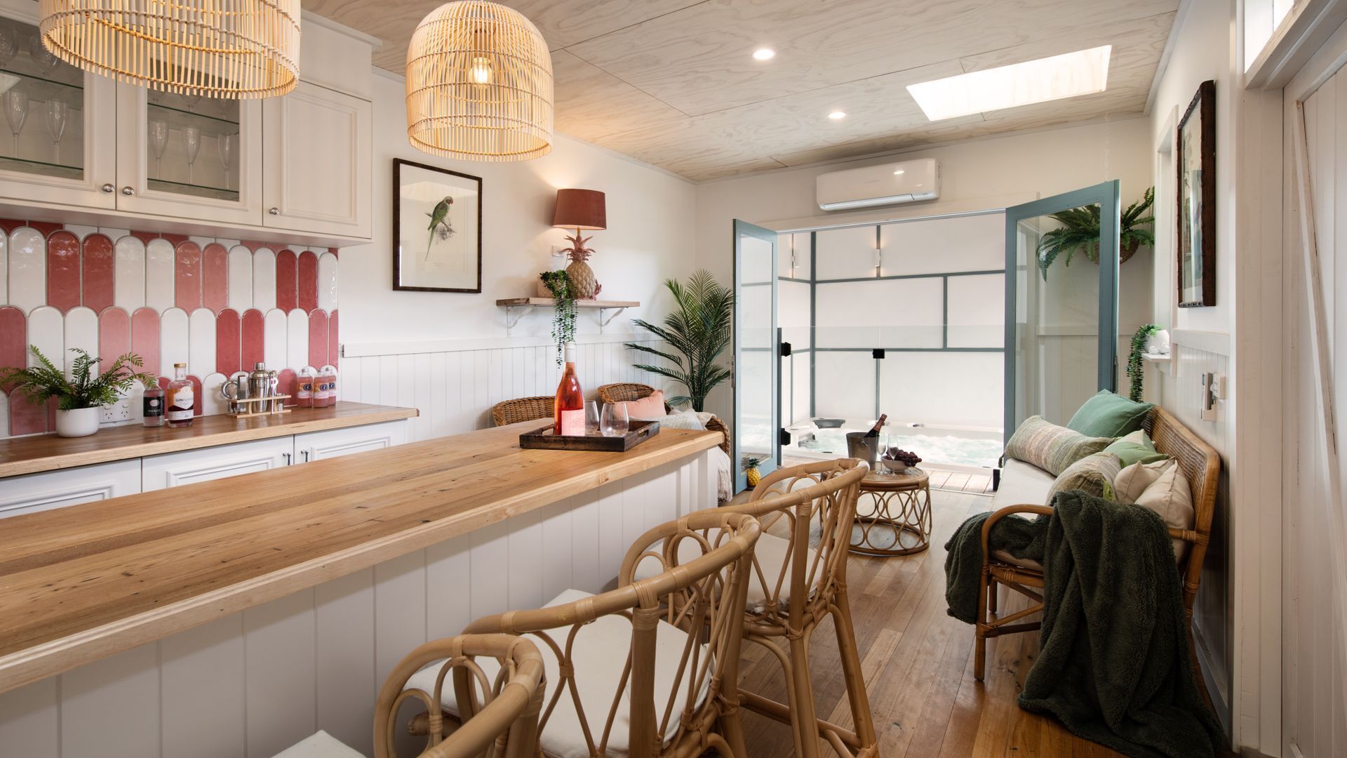 Une cuisine moderne avec des plans de travail en bois, des chaises en osier et une vue sur l’espace de vie.