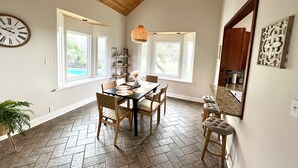 A dining area with a wooden ceiling, large windows, a herringbone tile floor, and a clock on the wall. - Scenic Lake View Home with Pool & Hot Tub (Bandera)