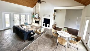 A spacious living room with a fireplace, a ceiling fan, and a dining area with wicker chairs. - Scenic Lake View Home with Pool & Hot Tub (Bandera)