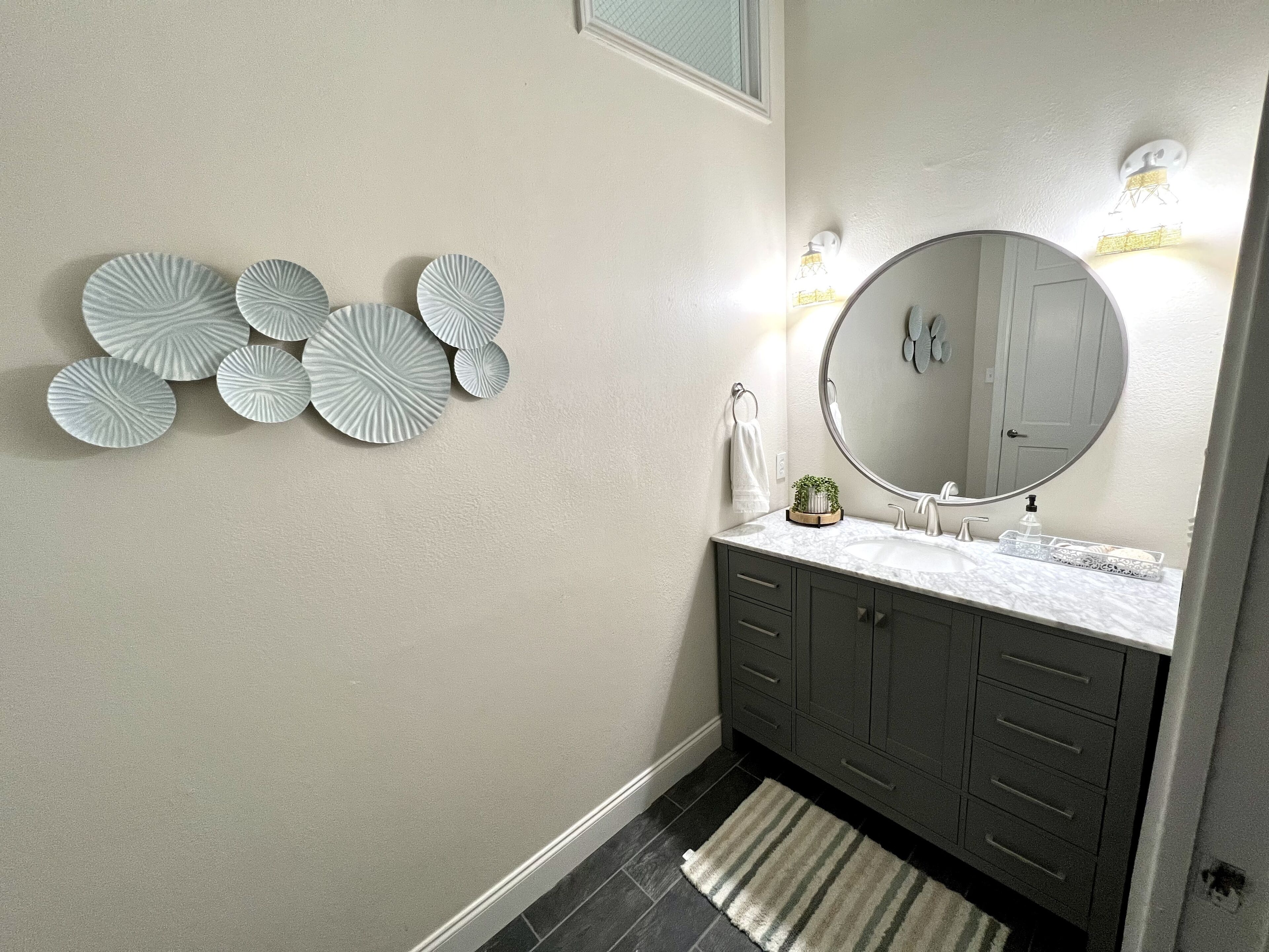 A bathroom with a round mirror, a sink with a marble countertop, and decorative wall plates.