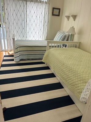 A bedroom with a bed, a bedside table, a lamp, and a window with curtains. - Adorable Beach house with lots of outdoor space and steps to Long Beach!  (Rockport)
