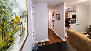 A living room with a large painting, a wooden floor, a black coffee table, and a beige sofa. - Central Stay! Near UK/Downtown/Campus. (Lexington)