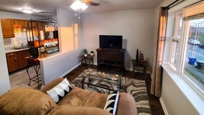 A living room with a sofa, a coffee table, a TV, and a kitchen area in the background. - Central Stay! Near UK/Downtown/Campus. (Lexington)