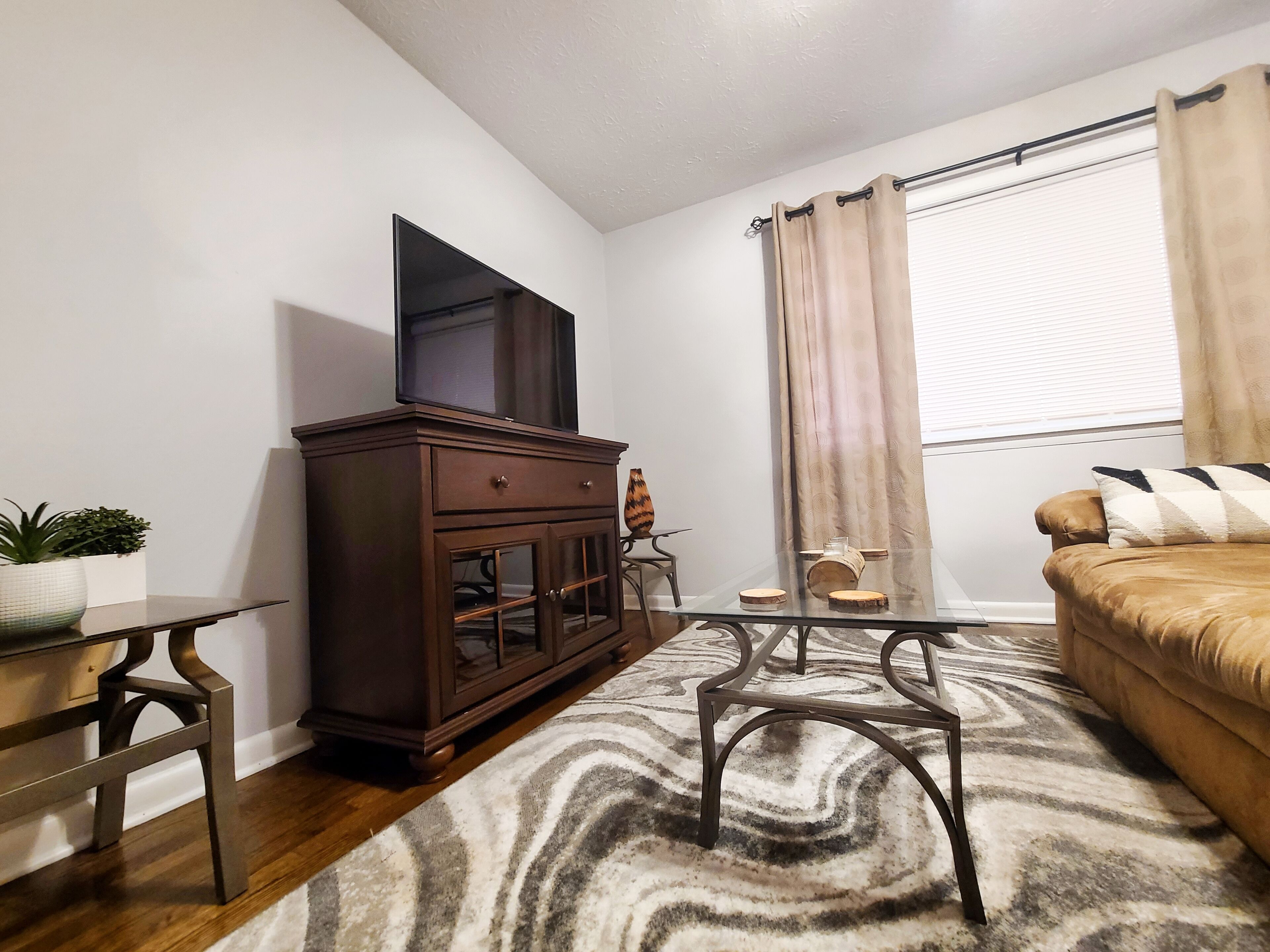 A living room with a dark wooden cabinet, a glass-top coffee table, a beige sofa, and a patterned rug.