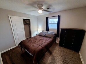 Ein Schlafzimmer mit Bett, Kleiderschrank, Deckenventilator und einem Fenster mit Vorhängen.