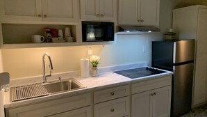 Une cuisine avec des armoires blanches, un évier en acier inoxydable, un réfrigérateur noir et un four à micro-ondes placé au-dessus de la cuisinière.