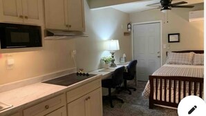 Une chambre avec un lit, un bureau et une chaise. La cuisine est équipée d’un four à micro-ondes et d’une cuisinière.