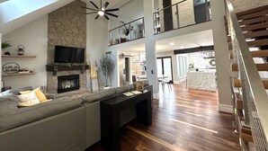 A spacious living area with a stone fireplace, a large sofa, and a modern ceiling fan. - High-end home w/ fireplace, gourmet kitchen, sauna, game rm/ large yard/fire pit (Mason)