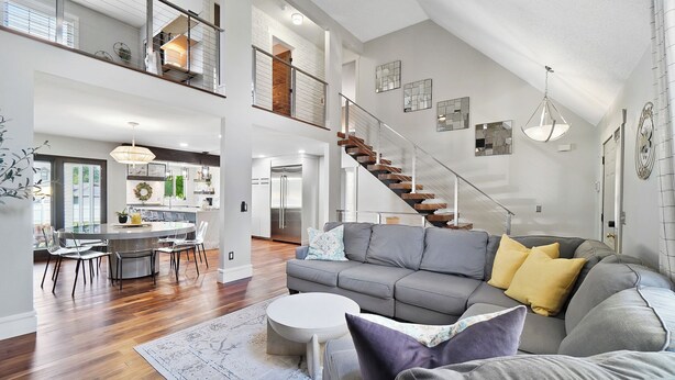 A spacious living area with a grey sofa, wooden flooring, and a staircase leading to an upper level. - High-end home w/ fireplace, gourmet kitchen, sauna, game rm/ large yard/fire pit (Mason)