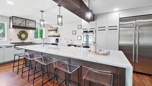 A modern kitchen with a large island, stainless steel appliances, and clear bar stools. - High-end home w/ fireplace, gourmet kitchen, sauna, game rm/ large yard/fire pit (Mason)