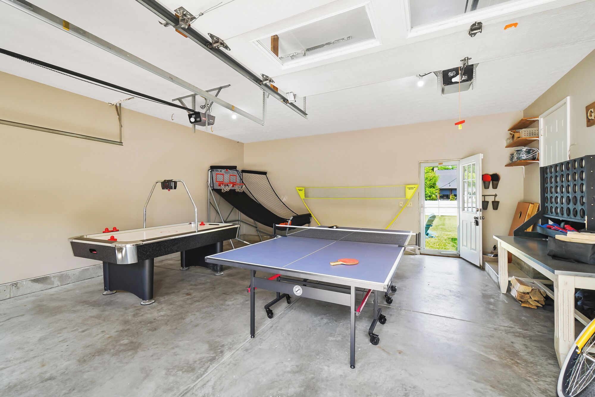 A room with a ping pong table, a foosball table, and a basketball hoop.