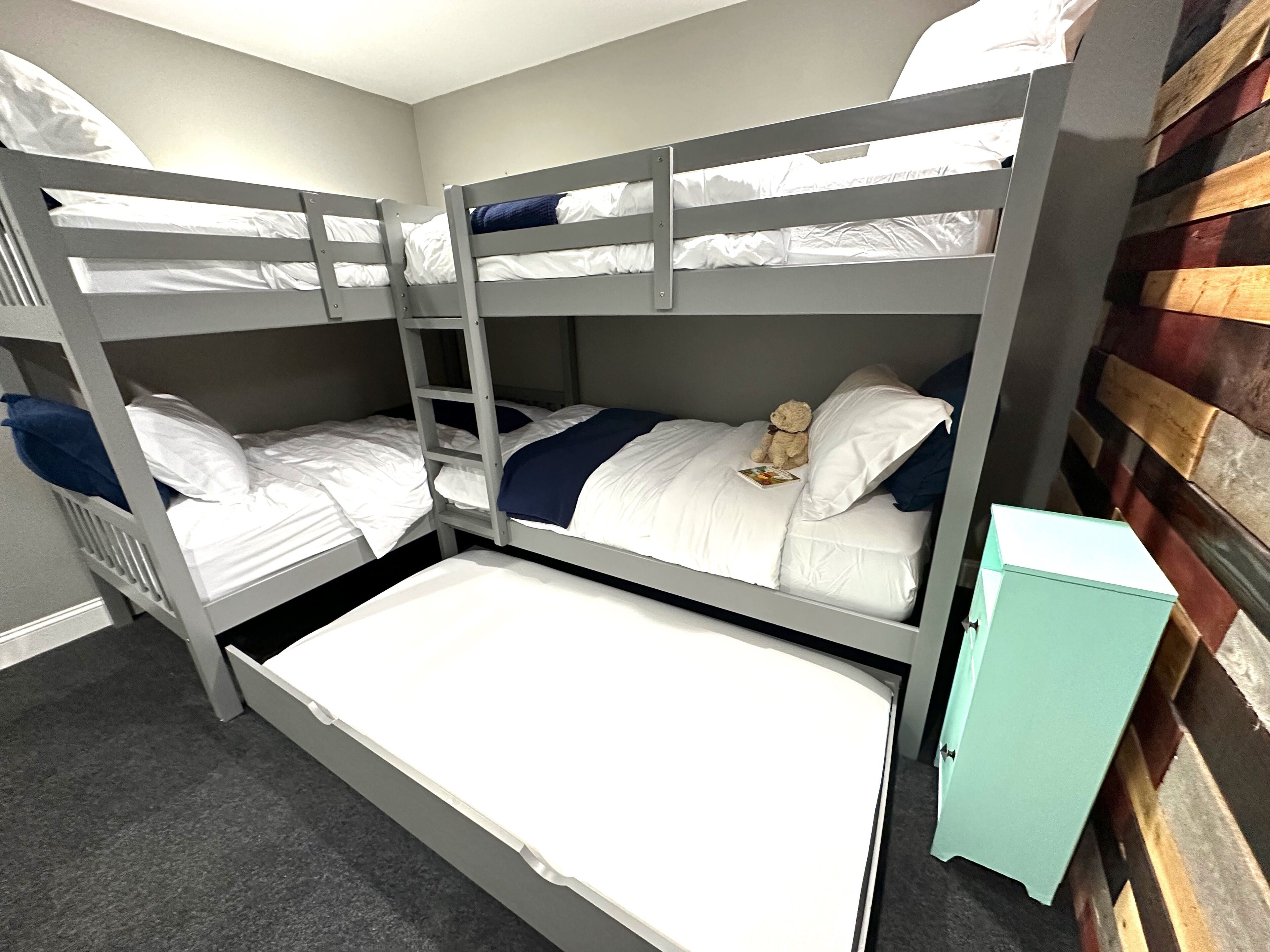 Une chambre avec un lit superposé, une échelle, une petite armoire et un ours en peluche sur le lit supérieur.