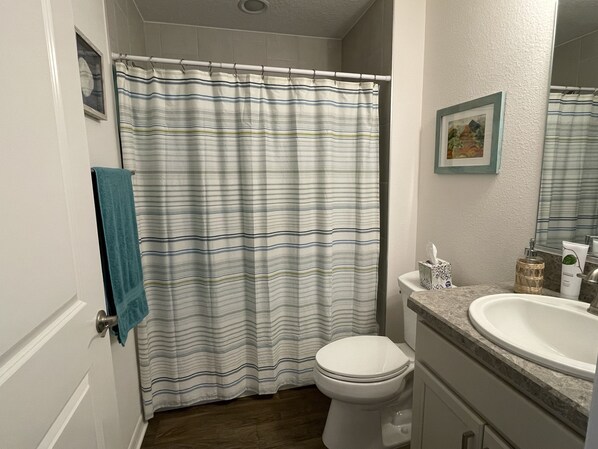 A bathroom with a striped shower curtain, a white toilet, a sink with a marble countertop, and a framed picture on the wall.