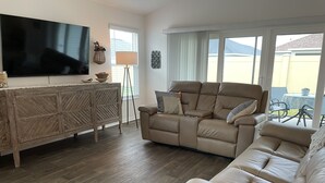 Uma sala de estar com uma televisão de tela plana grande, um sofá bege e um armário de madeira.