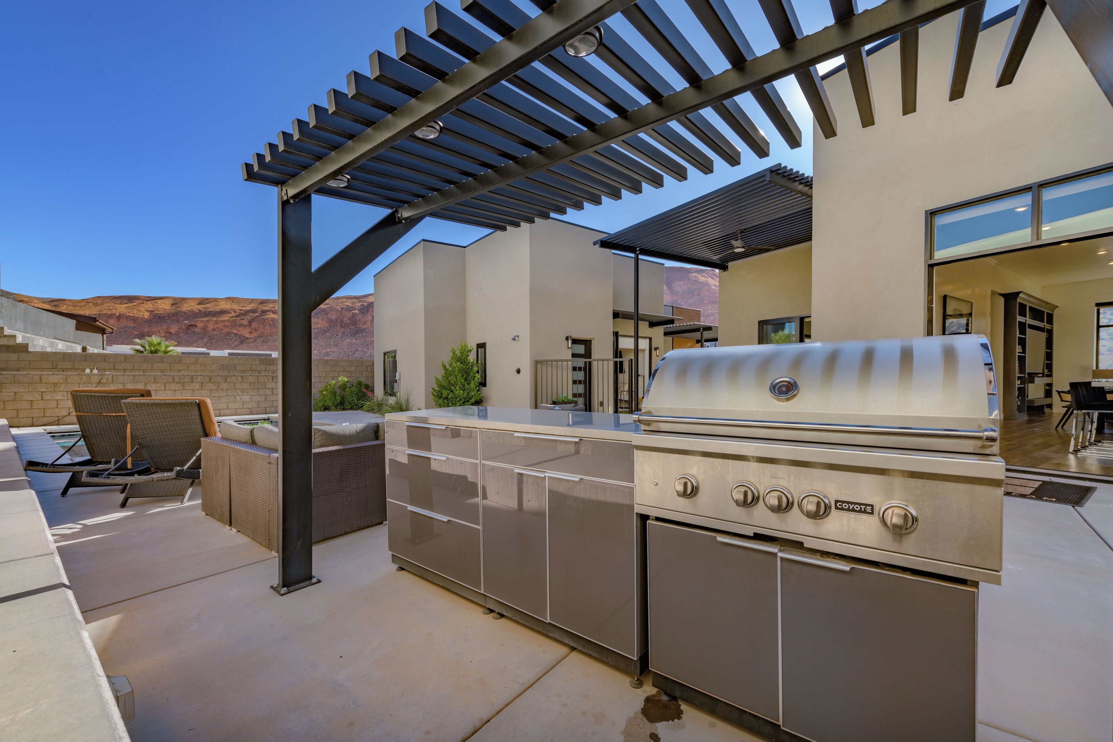 Ein Outdoor-Kochbereich mit Grill, Sitzgelegenheit und einer Pergola.