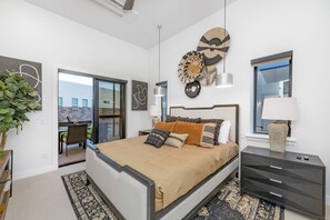 A modern bedroom with a large bed, a nightstand, a wall-mounted lamp, and a decorative wall piece. - Paradise Retreat at Copper Rock! (Hurricane)