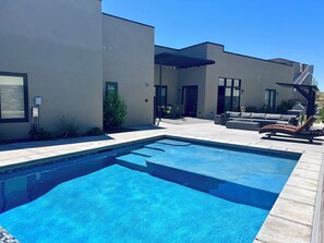 A modern outdoor pool area with a rectangular pool, a covered seating area, and a patio with a sofa and chairs. - Paradise Retreat at Copper Rock! (Hurricane)