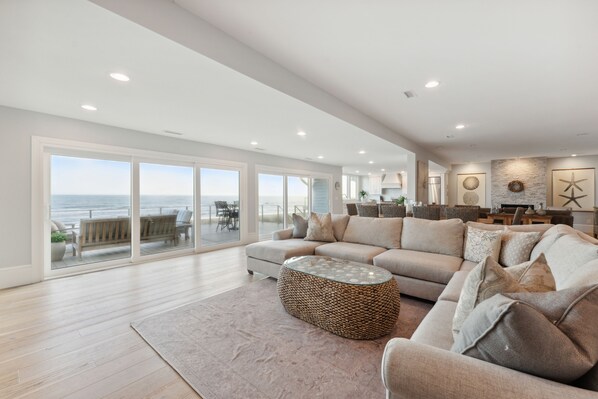 A spacious living room with a large sofa, a round coffee table, and a view of the ocean through large sliding doors.