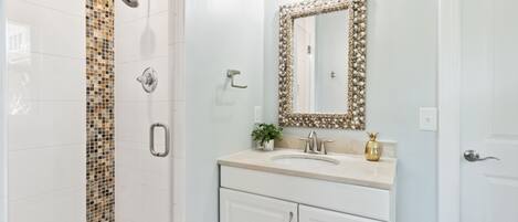 A bathroom with a shower, a sink with a decorative mirror, and a cabinet.
